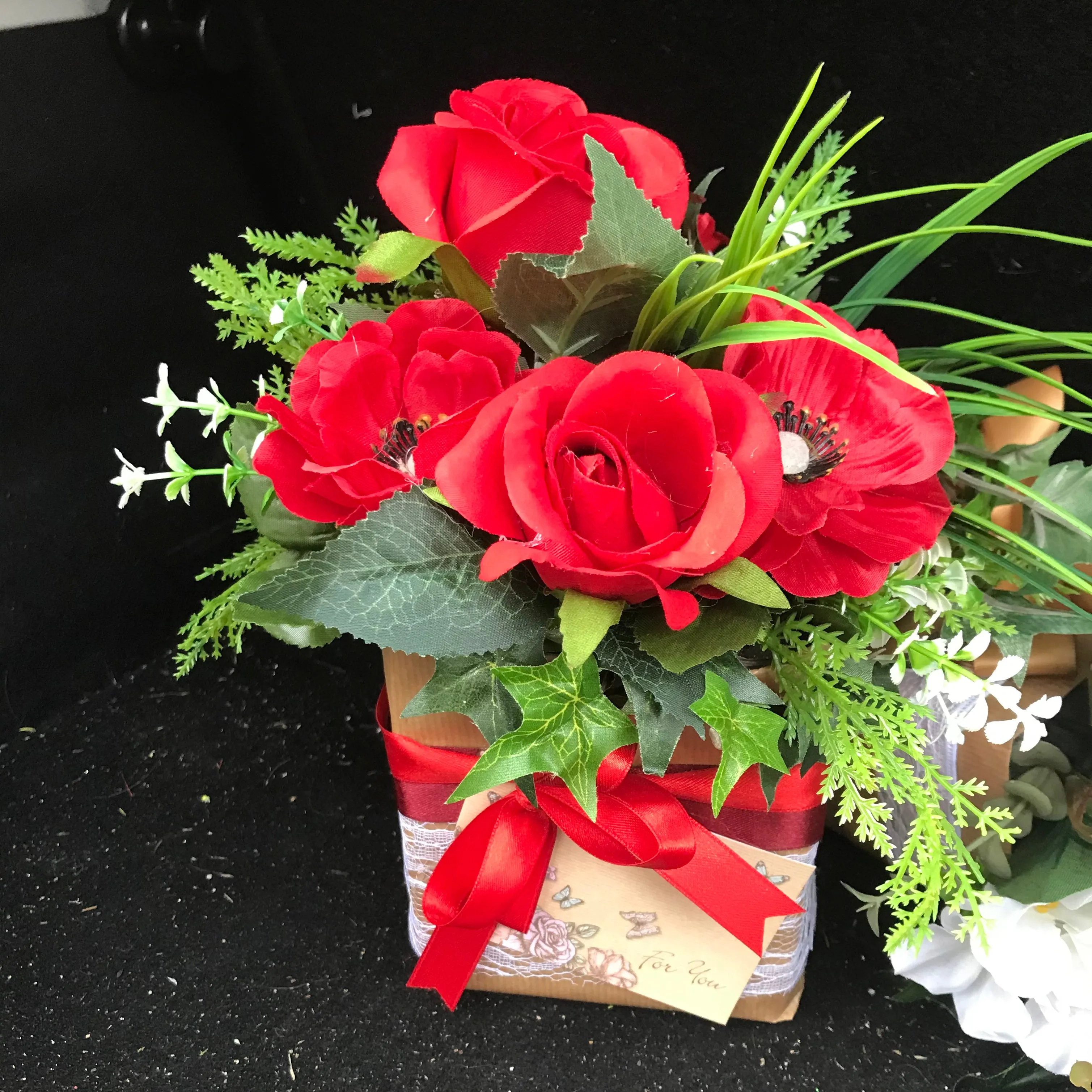 flower arrangement of artificial red anenomies & ivy in a gift bag